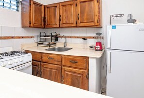 Une cuisine avec des meubles de rangement en bois, une cuisinière à gaz, un évier, un mixeur et un réfrigérateur.