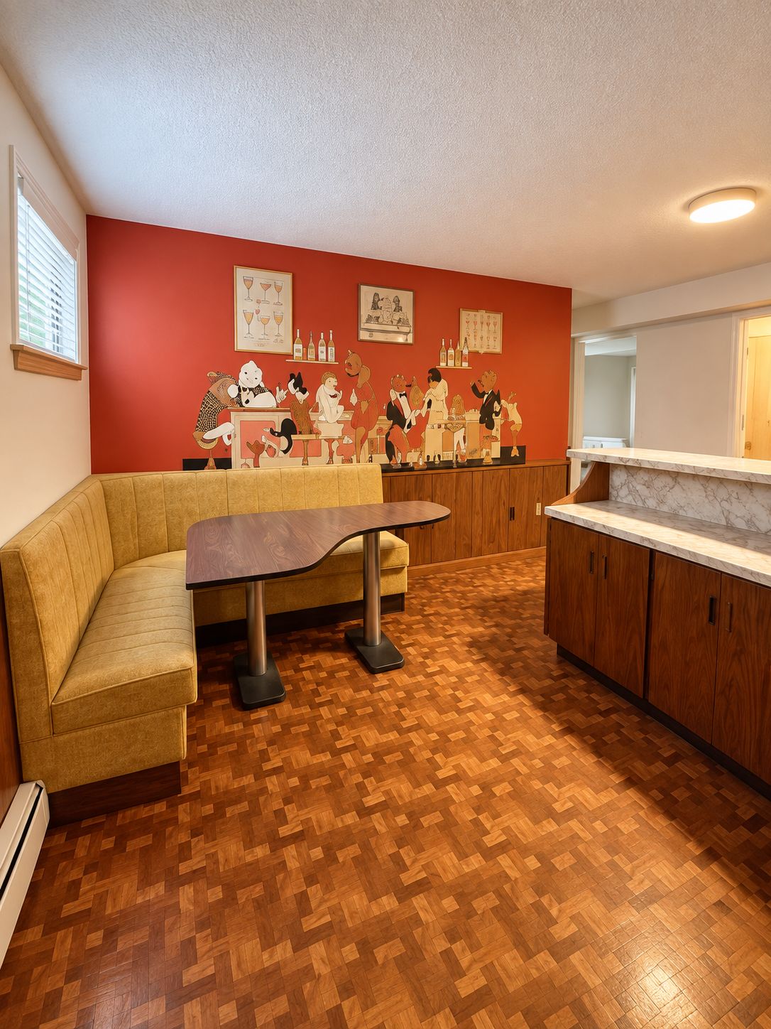 Una habitación con suelo de parqué de madera, un sofá color beige, una mesa con patas de metal y una pared de acento roja con obras de arte enmarcadas.
