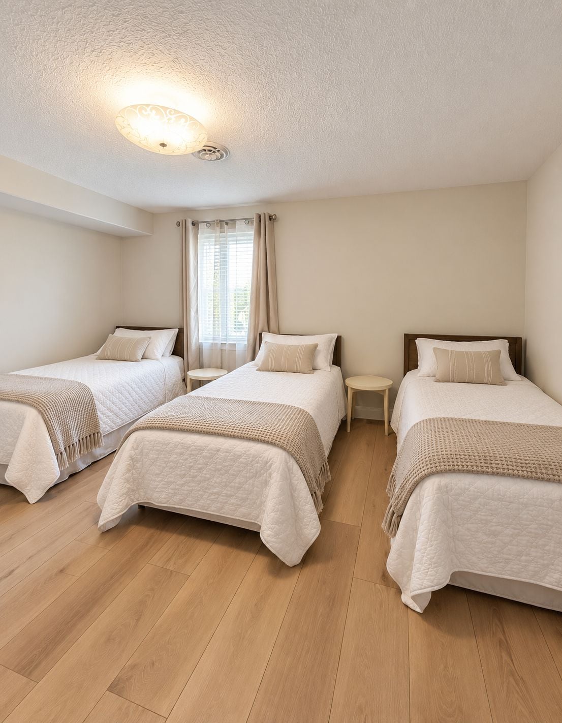 A hotel room with three single beds, a small table between each bed, and a ceiling light fixture.