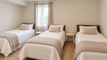 A hotel room with three single beds, a small table between each bed, and a ceiling light fixture.