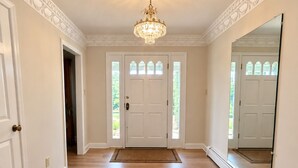 A hallway with a wooden floor, a white door with glass panels, and a large mirror on the right wall.