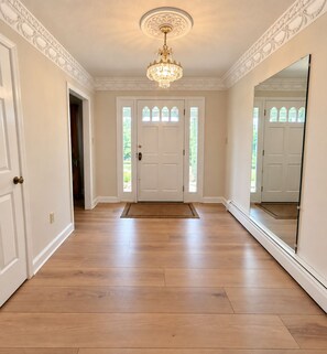 A hallway with a wooden floor, a white door with glass panels, and a large mirror on the right wall.