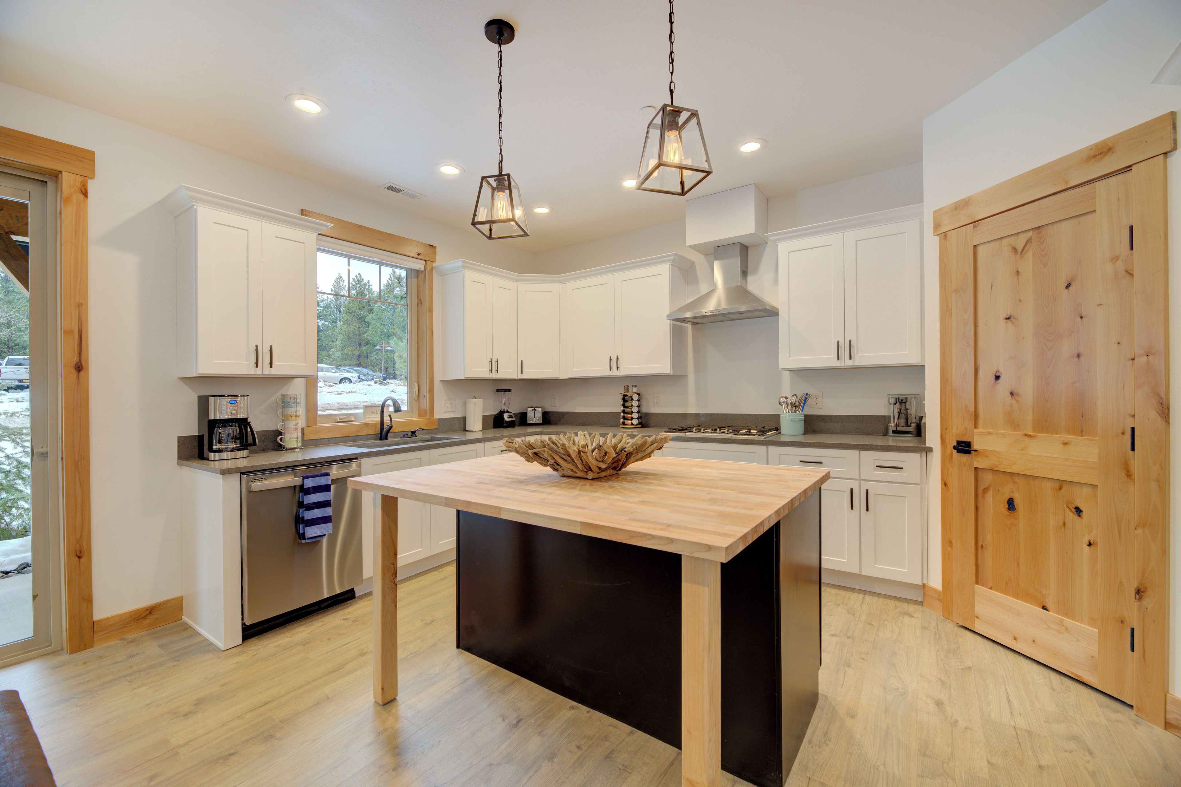 A modern kitchen with white cabinets, a central island, and a wooden door.