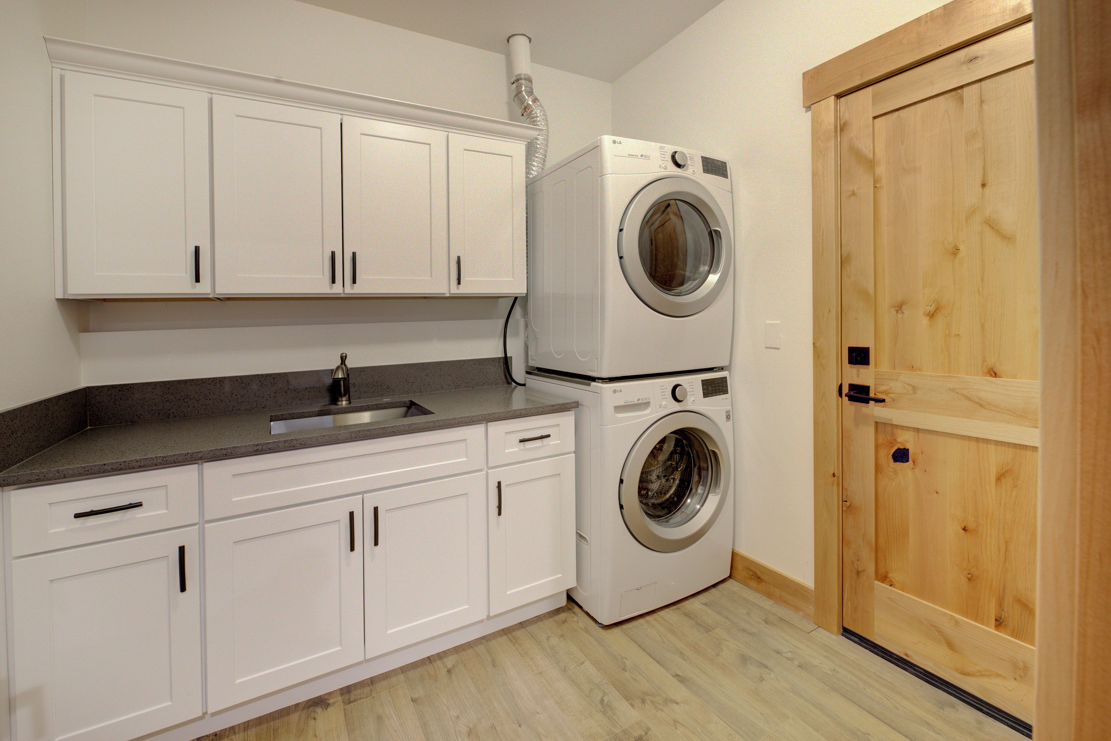 A laundry room with a washing machine and dryer, white cabinets, a sink, and a wooden door.