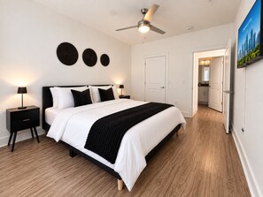 Ein Schlafzimmer mit einem Bett, Nachttischen, einem Deckenventilator und einer Tür zu einem Badezimmer.