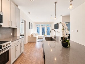 Et moderne køkken med en central ø, integrerede hårde hvidevarer og et spiseområde med en sofa.