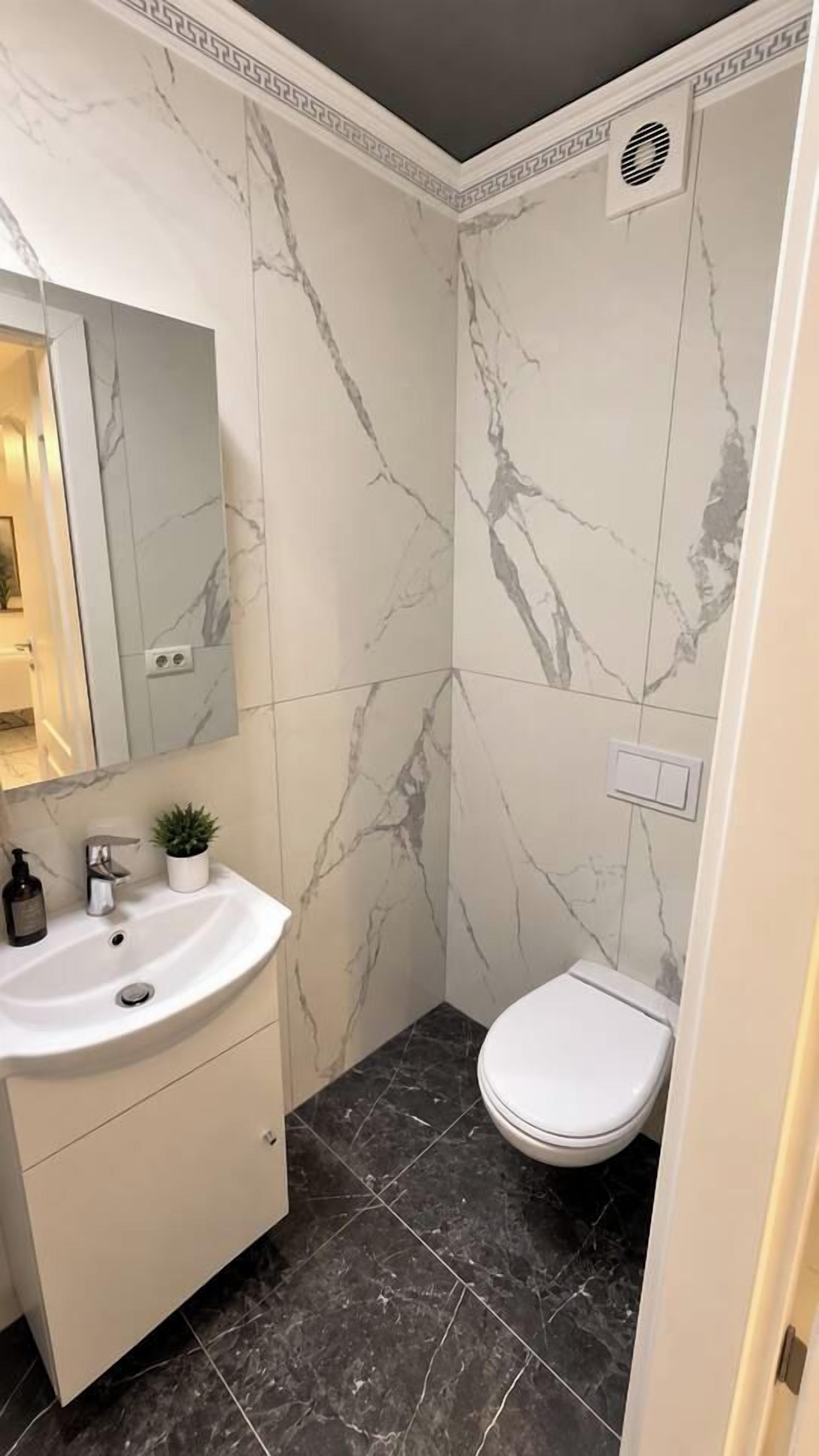 Une salle de bain avec un mur en marbre, un lavabo blanc, des toilettes et un miroir.