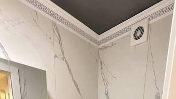Une salle de bain avec un mur en marbre, un lavabo blanc, des toilettes et un miroir.