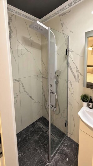 A modern bathroom with a glass-enclosed shower, marble walls, and a white sink. - Modern Studio | Central Bucharest (Bucharest)