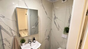 Een badkamer met een marmeren wand, een wastafel, een toilet en een spiegel.