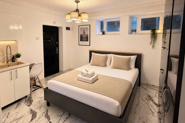 A modern hotel room with a large bed, a bathroom with a shower, a sink, and a small window. - Modern Studio | Central Bucharest (Bucharest)
