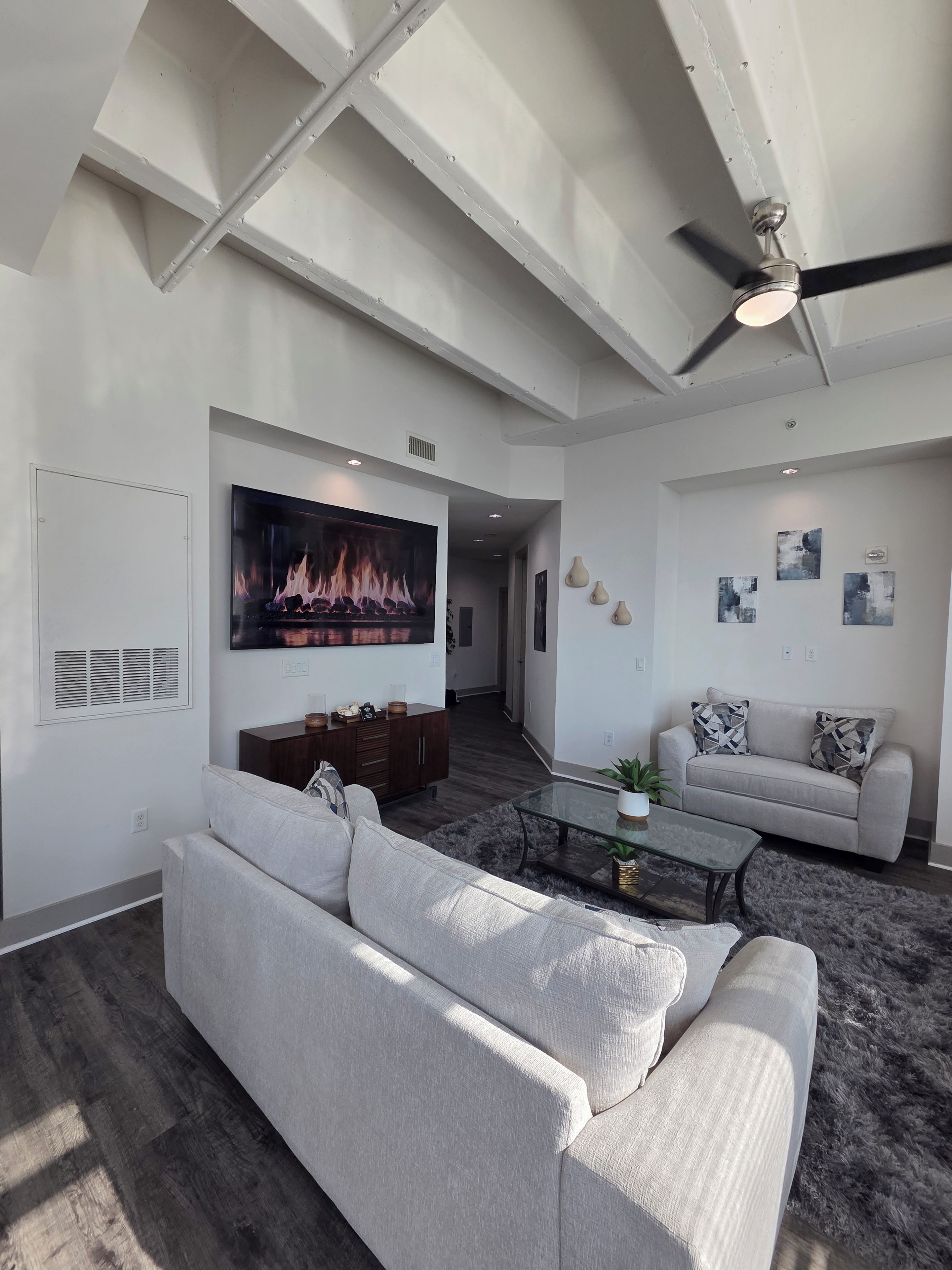 Un salon moderne avec un grand téléviseur à écran plat, un ventilateur de plafond et un canapé gris.