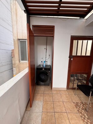 A small enclosed space with a washing machine, a chair, and a door leading to an outdoor area. - Carmen's House (Miraflores)
