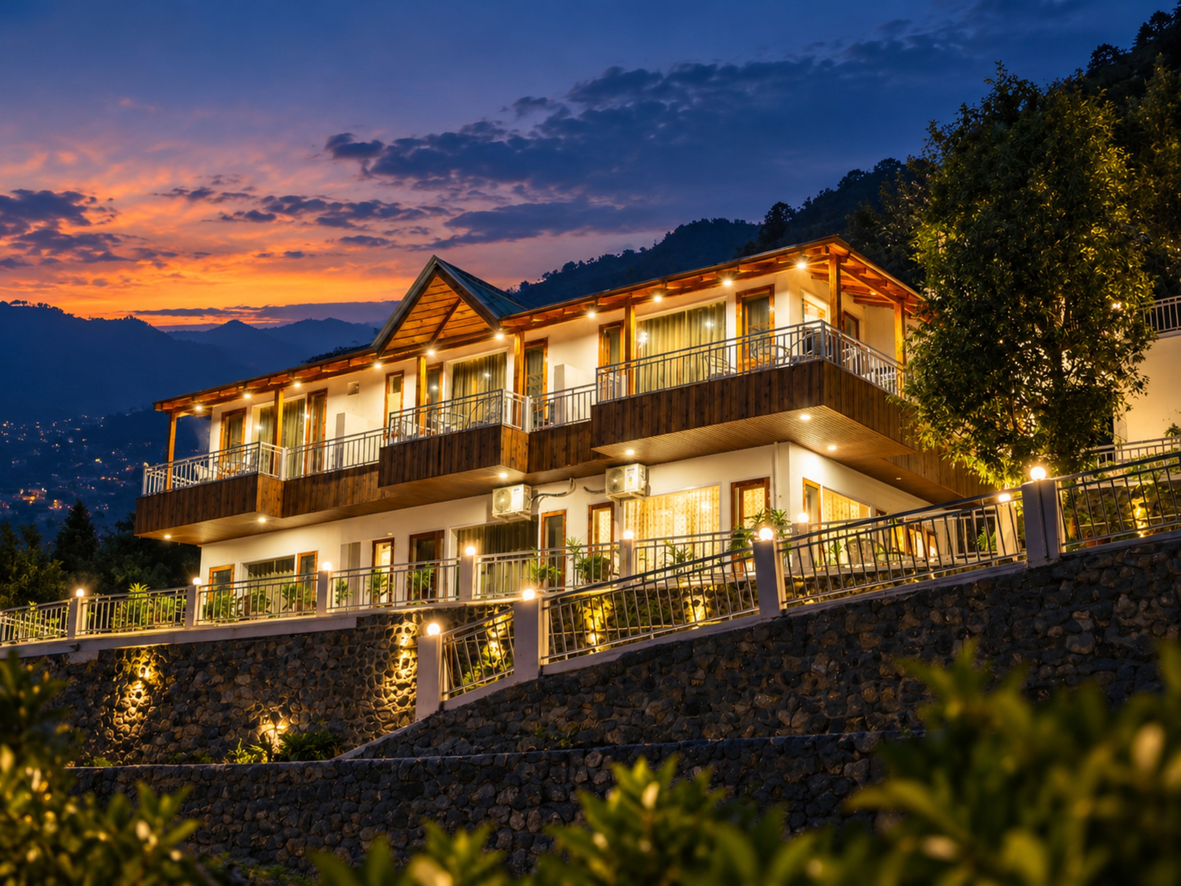 A multi-story hotel with balconies, stone walls, and a view of the mountains.