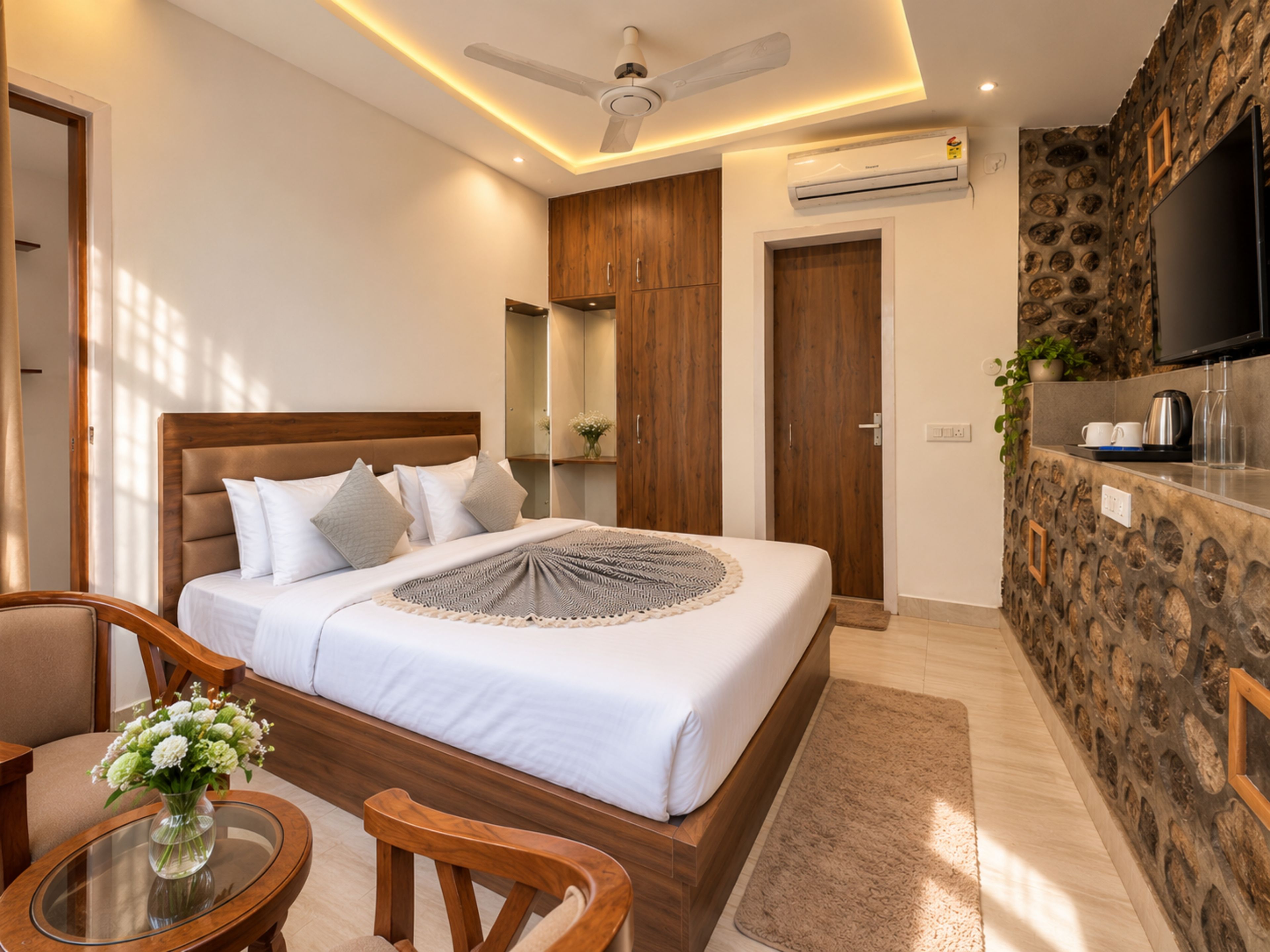 A hotel room with a bed, a seating area with a table and chairs, a television, and a stone accent wall.