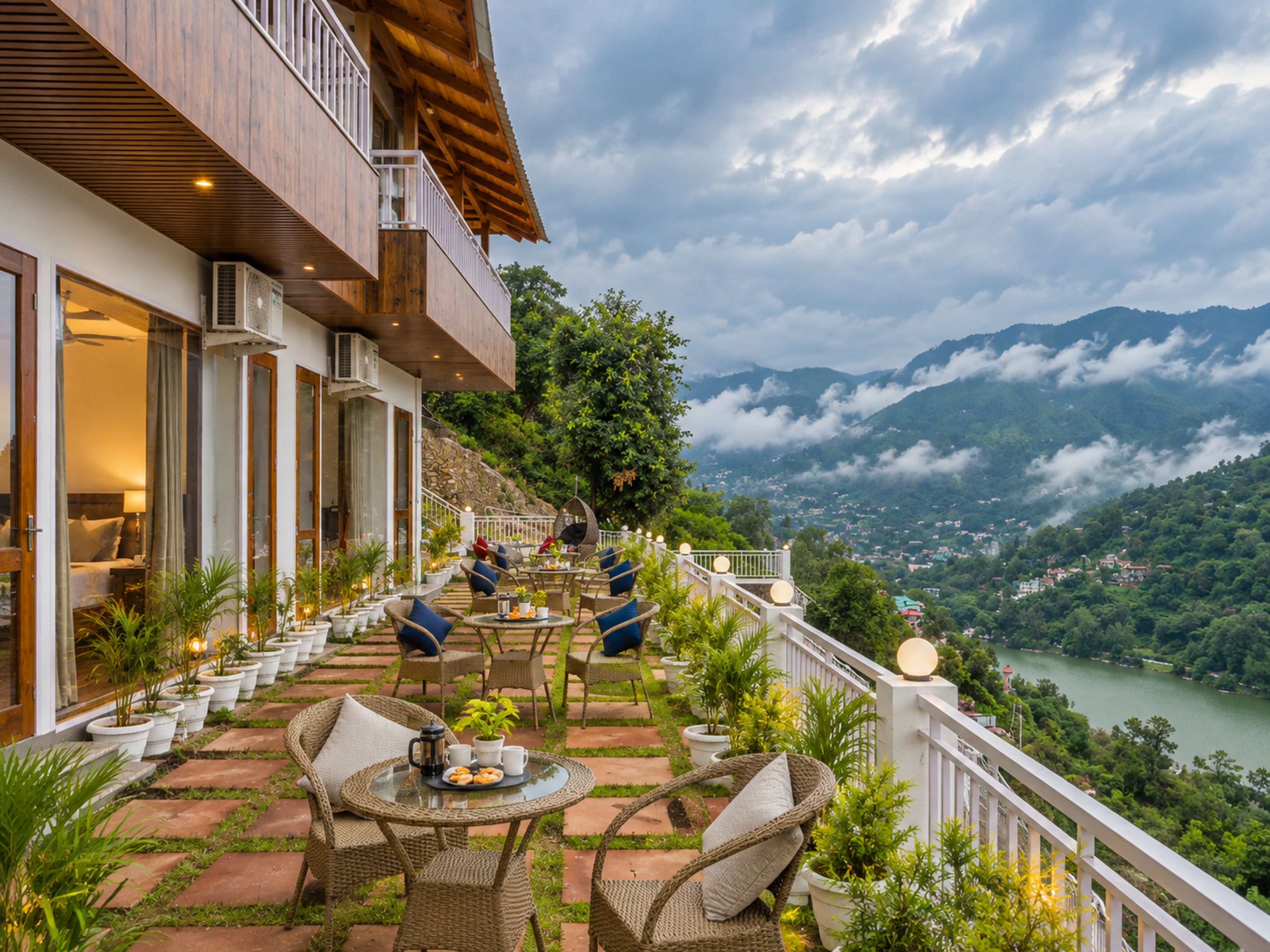 A hotel balcony with outdoor seating, a view of a lake, and mountains in the background.