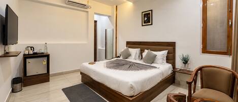 A hotel room with a bed, bedside table, chair, television, and a small refrigerator.