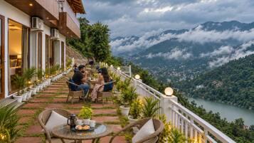 A terrace with wicker furniture, potted plants, and a view of a lake and mountains.