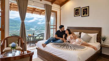 A bedroom with a wooden ceiling, a bed with white bedding, a view of mountains, and a dining area with a table and chairs.