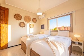 A hotel room with a large window, two beds, a wooden door, and wall decorations. - Majorelle Retreat Marrakech City Center (Marrakech)