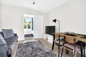Ein modernes Wohnzimmer mit einer Couch, einem Esstisch, einem Fernseher und einem großen Fenster.