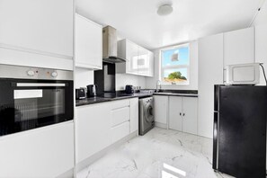 Eine moderne Küche mit weißen Schränken, einem schwarzen Backofen, einer Edelstahl-Waschmaschine und einem schwarzen Kühlschrank.