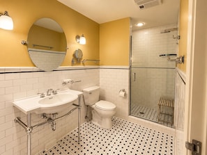 Un baño con lavamanos blanco, inodoro y zona de ducha con mampara de cristal.