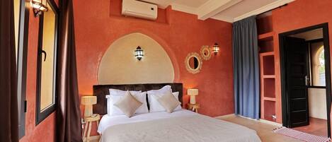 A hotel room with a large bed, two bedside lamps, a wall-mounted air conditioner, and a decorative mirror.