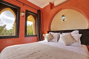 A hotel room with a large bed, two wall-mounted lamps, and a view through an arched window. - Domaine Zayna (Marrakech)
