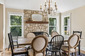 A dining room with a stone fireplace, a chandelier, and a view of the outdoors through large windows.