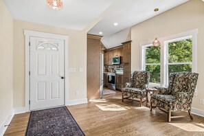 A hallway with a wooden floor, a white door, and two patterned armchairs.