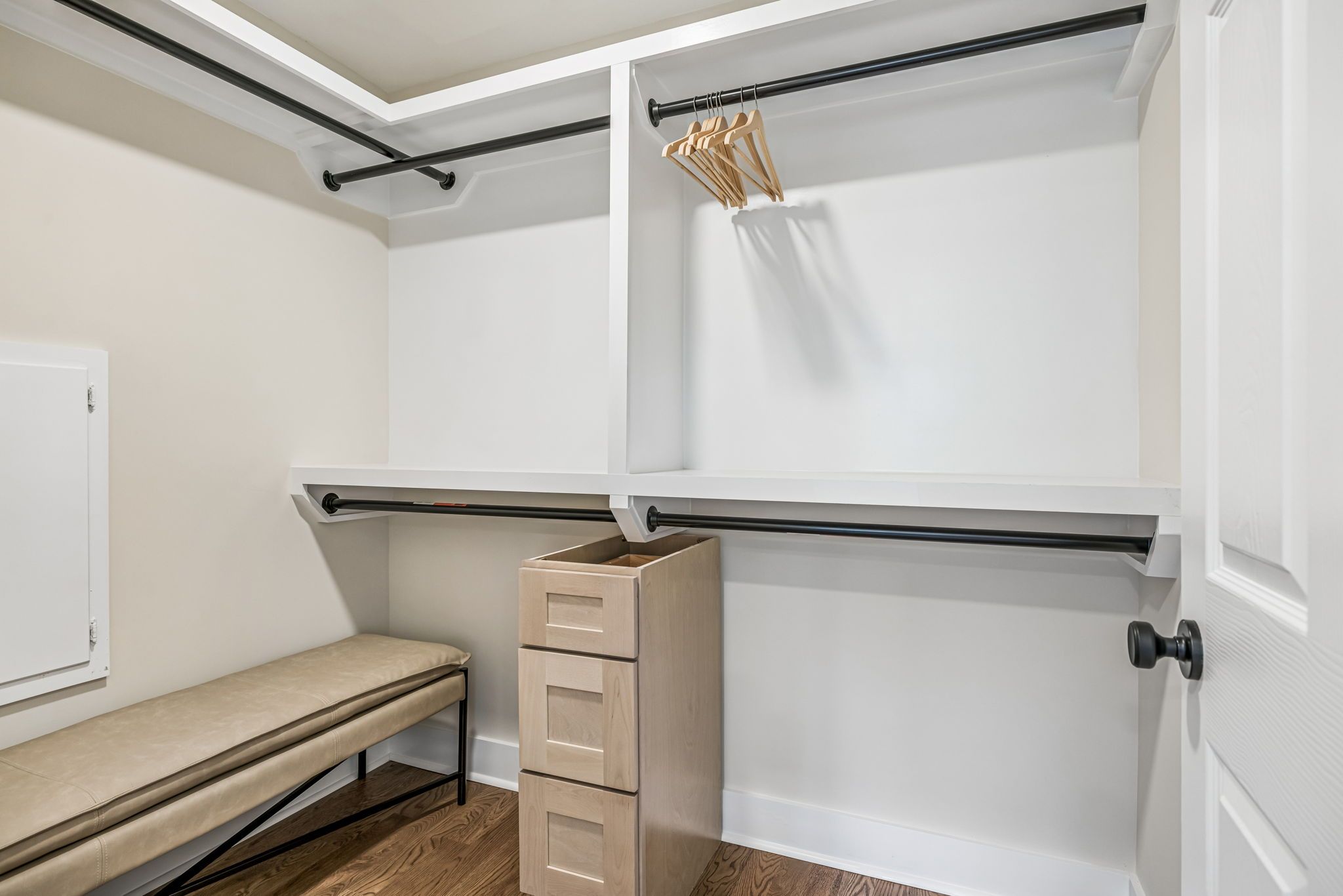 Un vestidor amplio con un banco, una serie de cajones y una barra para colgar ropa con perchas de madera.