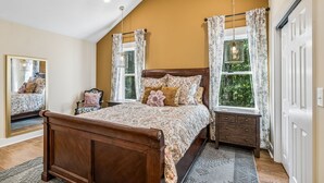Un dormitorio con cama de madera, mesita de noche, espejo y ventana con cortinas.