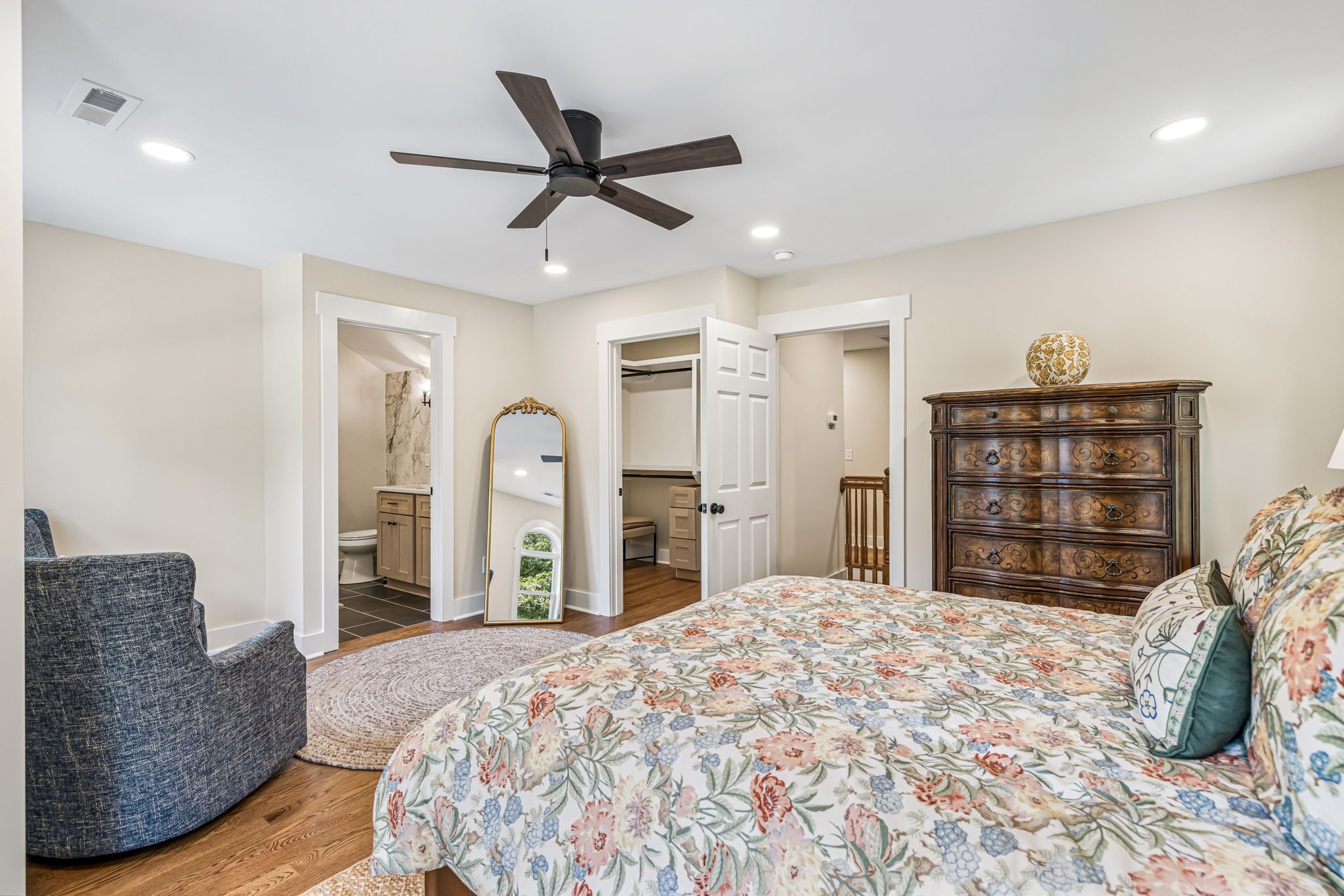A bedroom with a bed, dresser, chair, and a ceiling fan.