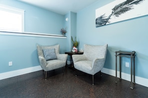 A room with two grey upholstered chairs, a small round table with a vase and books, and a metal side table.