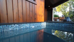 Una piscina cristalina con borde de azulejos, paredes de madera y vistas a árboles y un edificio al fondo.