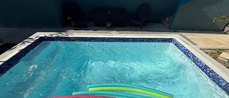 A rectangular swimming pool with a tiled edge, surrounded by a concrete deck.