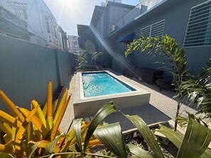 Une piscine de forme rectangulaire, entourée d’une terrasse en béton et bordée de murs.