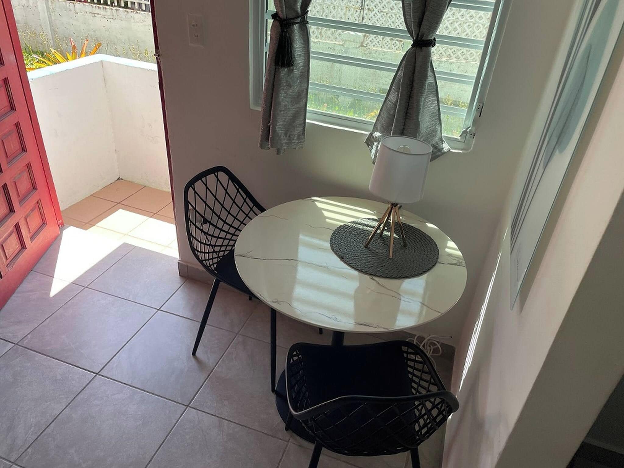 A small dining area with a round table, two chairs, a lamp, and a window with curtains.