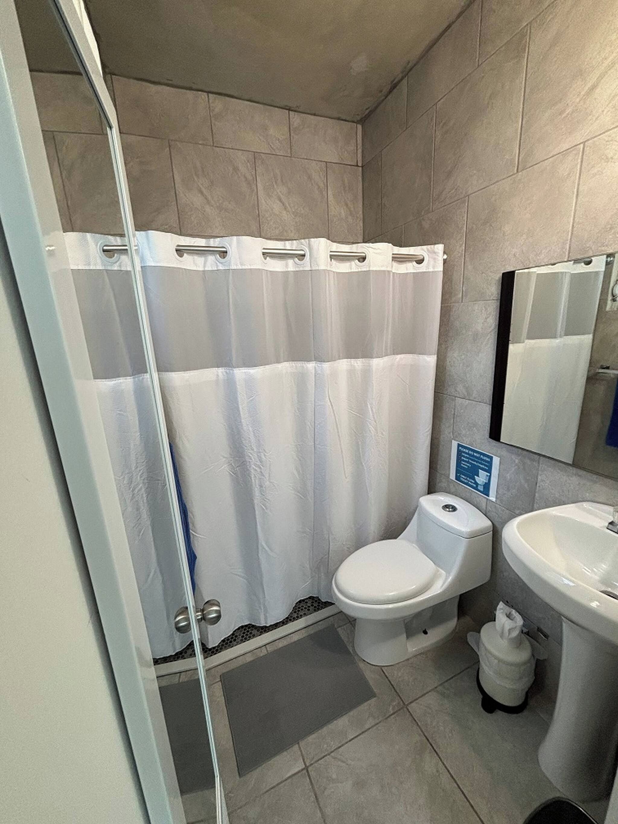 A bathroom with a shower curtain, toilet, sink, and a small trash bin.