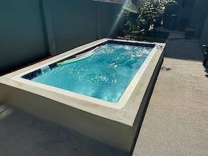 Una vasca idromassaggio esterna rettangolare con piscina azzurra trasparente, circondata da un pavimento in cemento e da un tappeto antiscivolo.