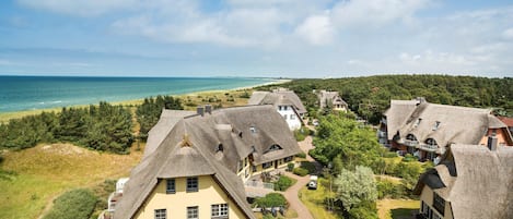 Uma vila costeira com casas de campo tradicionais com telhados de palha, vista clara para o mar e um morro arborizado.