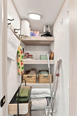 A compact kitchen with wooden shelves, a hanging pot rack, and storage baskets. - Glamping Getaway - On the 290 Wine Trail (Fredericksburg)