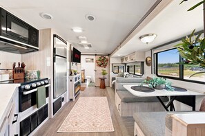 A modern RV interior with a kitchen, dining area, and a large window offering a view. - Glamping Getaway - On the 290 Wine Trail (Fredericksburg)