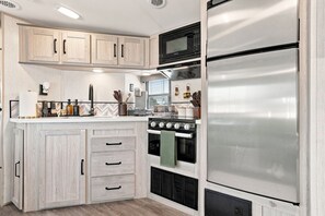 Une cuisine moderne avec des meubles en bois clair, un réfrigérateur en acier inoxydable, un four encastré et un four à micro-ondes.