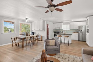 A spacious living area with a dining table, a gray sofa, and a kitchen in the background. - Lakeview Nook - 6 min to Cypress Creek Park (Austin)