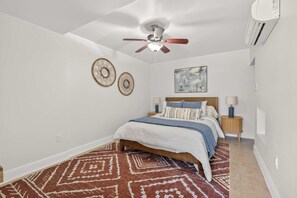 Ein Schlafzimmer mit einem Bett, einem Deckenventilator, zwei Wandspiegeln, einem Gemälde und einem gemusterten Teppich.