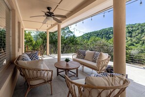 A covered outdoor seating area with wicker furniture, a ceiling fan, and a view of a forested hillside. - Lakeview Nook - 6 min to Cypress Creek Park (Austin)