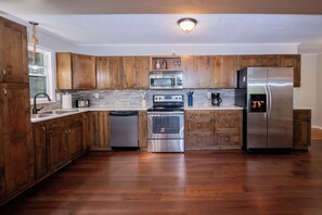 A modern kitchen with wooden cabinets, stainless steel appliances, and a dishwasher. - Watts Bar Lake House Retreat (Kingston)