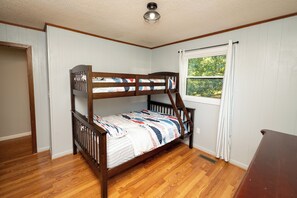 A bunk bed with a patterned bedspread, a window with curtains, and wooden flooring. - Watts Bar Lake House Retreat (Kingston)